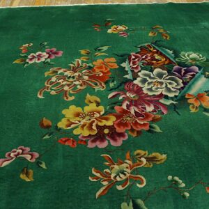 Deep green rug with a central multi-color floral bouquet on light wood planks.