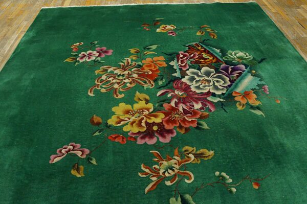Deep green rug with a central multi-color floral bouquet on light wood planks.