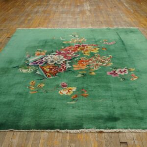 Bright green rug with large multicolored floral designs and white fringe lying on weathered wood planks.