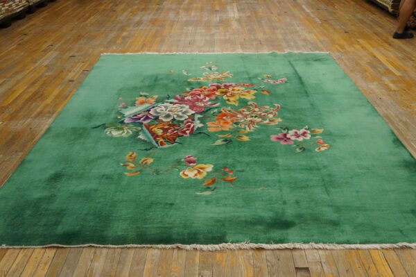 Bright green rug with large multicolored floral designs and white fringe lying on weathered wood planks.