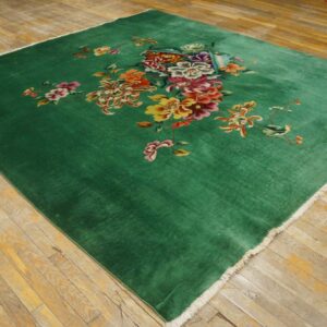 Plush green rug featuring an asymmetrical colorful floral design on yellowish wood planks.