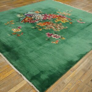 Bright multicolored flowers are centered on a plush emerald green rug over aged hardwood flooring.