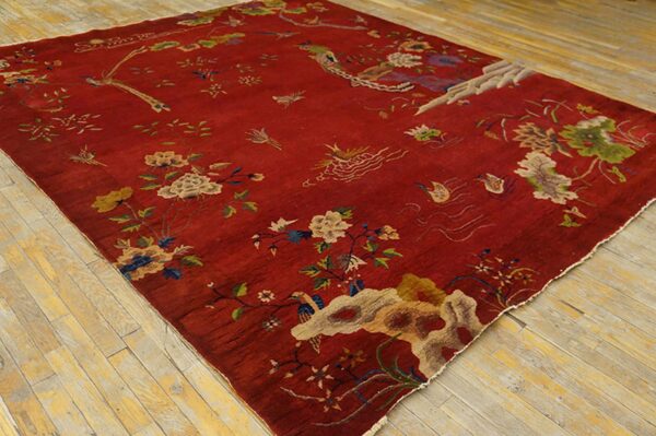Red, low pile rug featuring detailed beige, green, and blue floral and avian motifs on wood plank flooring.