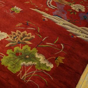 A deep red rug with an intricate floral and scenic pattern rests on worn yellow wooden floor planks.