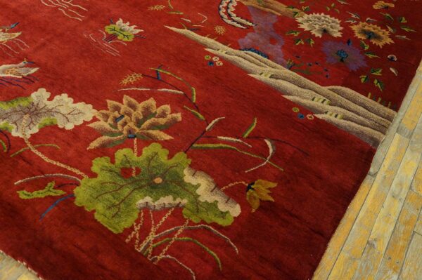 A deep red rug with an intricate floral and scenic pattern rests on worn yellow wooden floor planks.