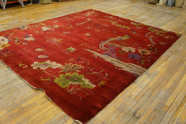 Low-pile red rug featuring detailed traditional floral and bird designs resting on light wood plank flooring.