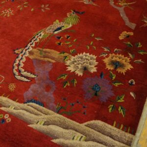 A red rug with an ornate pattern of birds and flowers rests next to distressed yellow wooden planks.