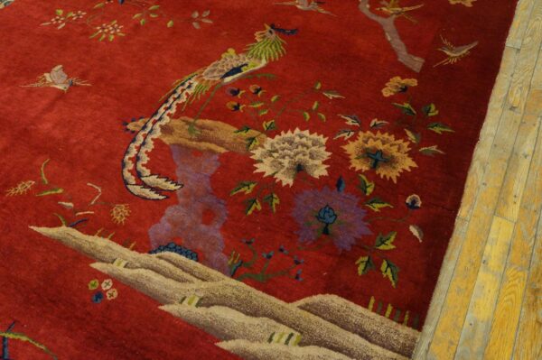A red rug with an ornate pattern of birds and flowers rests next to distressed yellow wooden planks.