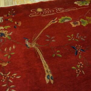 Deep red area rug with an intricate pattern of birds, flowers, and vines resting on plank flooring.