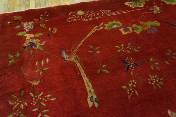 Deep red area rug with an intricate pattern of birds, flowers, and vines resting on plank flooring.