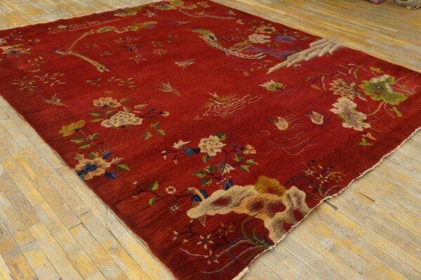 Deep red pictorial rug with multi-colored flowers and birds resting on light wooden plank flooring.