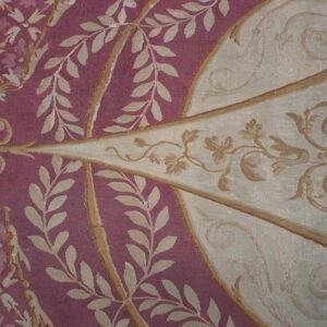 Ornate, low-pile rug detail in berry red and cream featuring classical scrolls and leaf motifs.