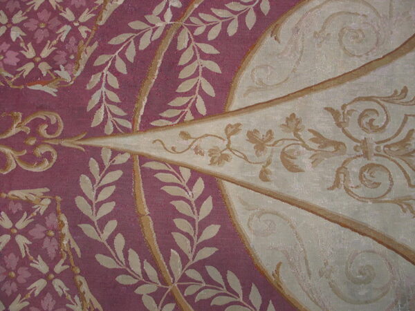 Ornate, low-pile rug detail in berry red and cream featuring classical scrolls and leaf motifs.