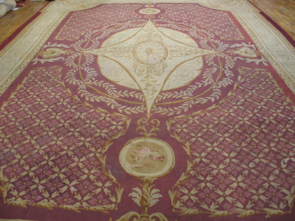Burgundy-pink and cream rug with a classical medallion and dense floral trellis pattern, shown on wood flooring.