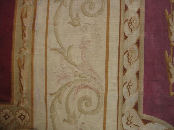 Tight weave rug with scrolling beige and tan motifs in striped panels next to a deep wine border.