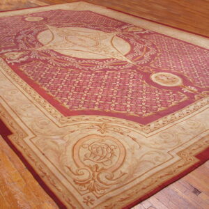 Ornate crimson and beige patterned area rug with a large medallion sits on plank wood flooring.