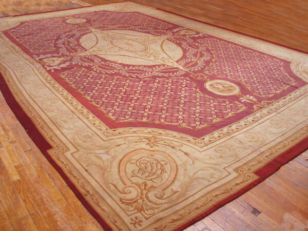 Ornate crimson and beige patterned area rug with a large medallion sits on plank wood flooring.