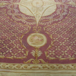 Large, elaborate low-pile rug in deep mauve and cream featuring detailed scroll and repeating floral motifs.