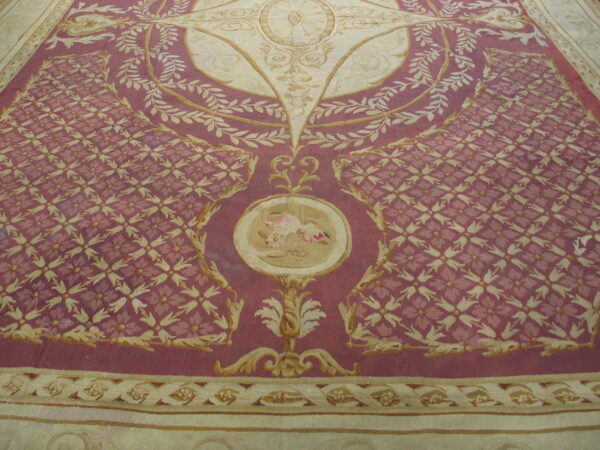 Large, elaborate low-pile rug in deep mauve and cream featuring detailed scroll and repeating floral motifs.