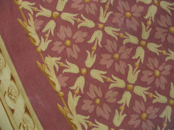 Stylized gold and pink floral patterns cover a maroon textile with a distinct scrolling border.