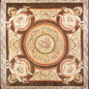 Square rug with a dark brown field patterned with cream ovals, pink florals, and a pale blue border.