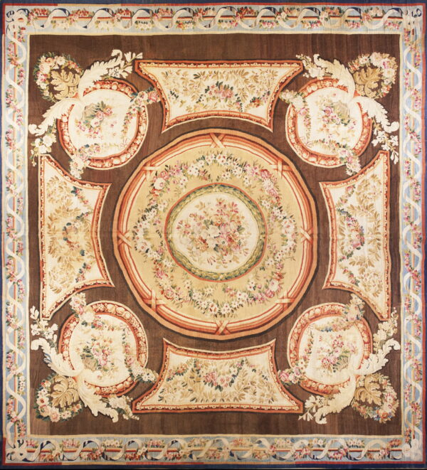 Square rug with a dark brown field patterned with cream ovals, pink florals, and a pale blue border.