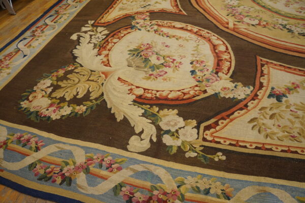Detailed floral rug featuring cream medallions on a brown ground, with a blue and ribbon border on wood floors.