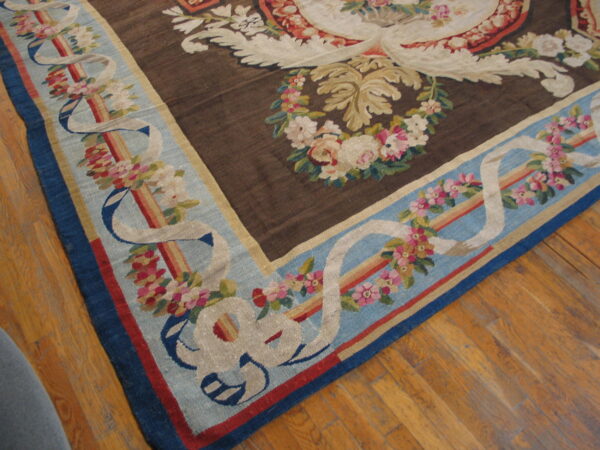 Dark brown and blue flat-weave rug with ornate floral patterns displayed on a hardwood floor.