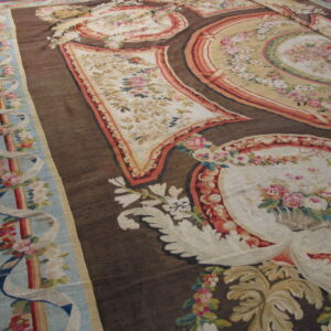 Low-pile rug with complex floral cartouches, cream panels, and a dark brown ribbed field on wood floor.