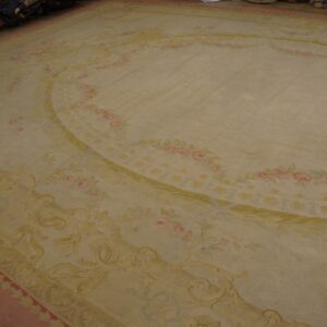 Cream-colored area rug featuring a central oval medallion and pink floral garlands with green leaves.