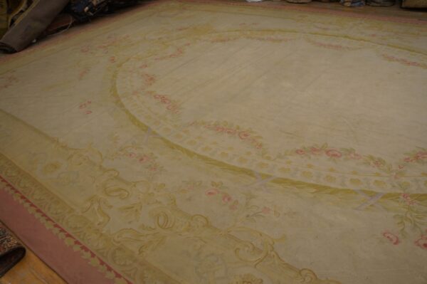 Cream-colored area rug featuring a central oval medallion and pink floral garlands with green leaves.