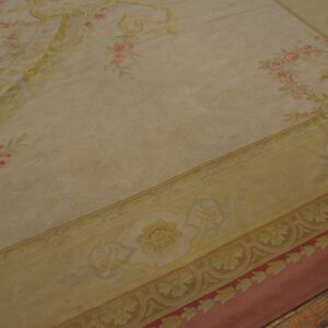 Low-pile cream rug featuring pink rose sprays and an ornate yellow border on distressed wood flooring.