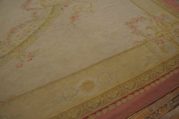 Low-pile cream rug featuring pink rose sprays and an ornate yellow border on distressed wood flooring.