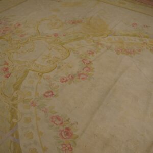 Large, low-pile rug with elaborate scrollwork and floral motifs in pale pink, yellow, and cream.