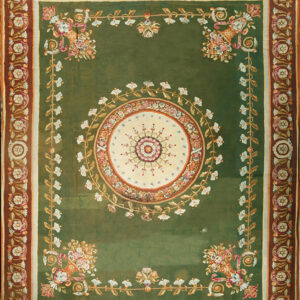 An elaborate sage green rug featuring a central floral medallion and wide multi-colored scrolled borders.