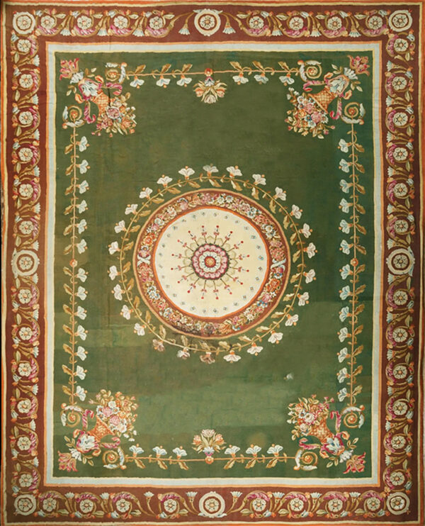 An elaborate sage green rug featuring a central floral medallion and wide multi-colored scrolled borders.