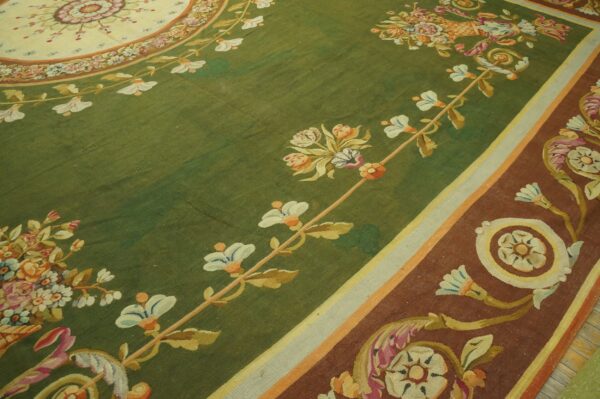 Detailed view of a classic rug featuring a green field, colorful floral motifs, and a wide rust-colored border.