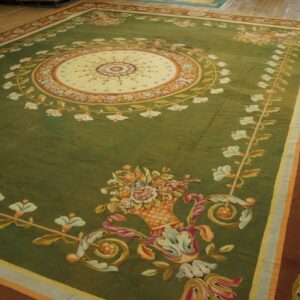A large olive green rug with a cream medallion and rust border featuring elaborate floral patterns on a wood floor.