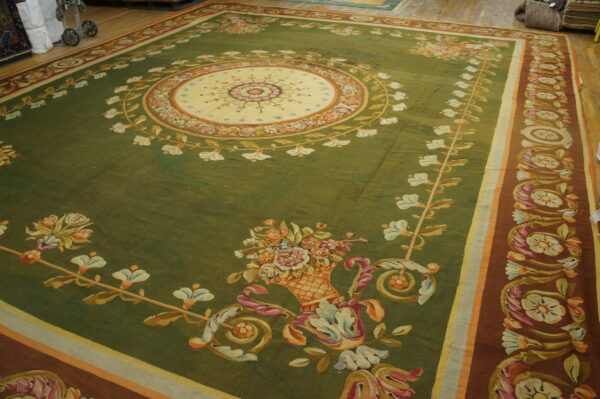 A large olive green rug with a cream medallion and rust border featuring elaborate floral patterns on a wood floor.