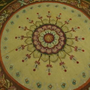 Low-pile floral rug featuring a central medallion on a pale yellow field and wide green and brown floral borders.