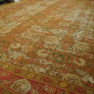 A heavily distressed orange and red floral rug with major wear holes displayed on wooden flooring.