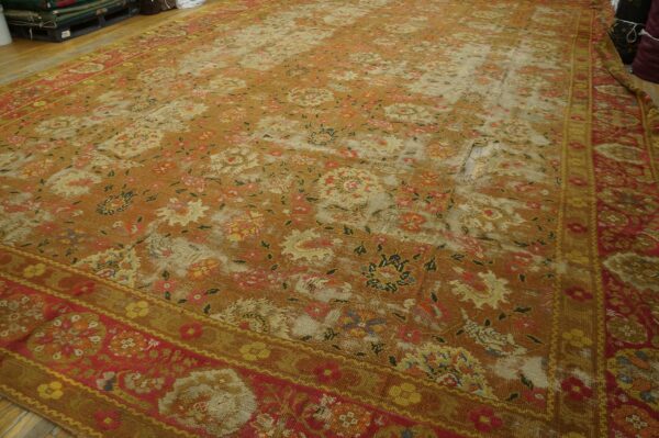 A heavily distressed orange and red floral rug with major wear holes displayed on wooden flooring.