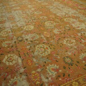 Low-pile rug with a faded rust and gold floral design, visible foundation threads, and pink borders.