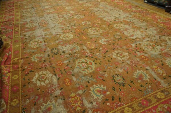 Low-pile rug with a faded rust and gold floral design, visible foundation threads, and pink borders.