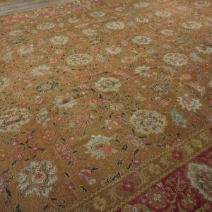 Low-pile tan rug featuring distressed multicolored floral motifs and a contrasting red and gold detailed border.