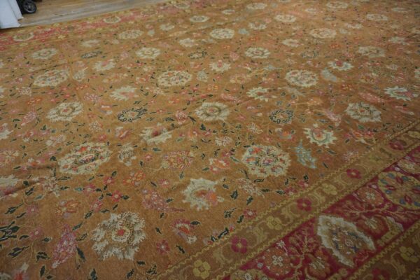 Low-pile tan rug featuring distressed multicolored floral motifs and a contrasting red and gold detailed border.
