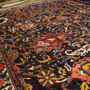 Dark-field rug featuring intricate red, yellow, and blue floral designs lies on a wood floor.