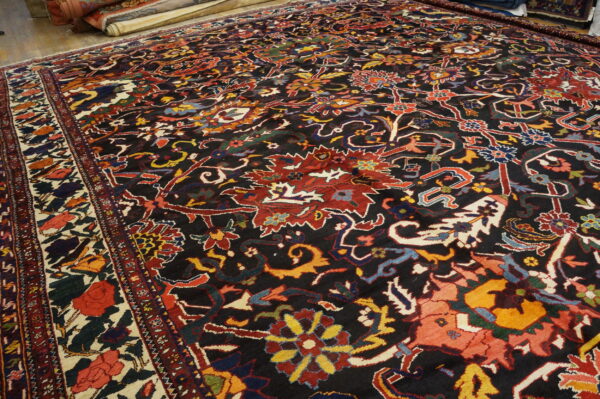 Dark-field rug featuring intricate red, yellow, and blue floral designs lies on a wood floor.