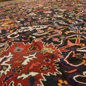 Detailed view of a dark, traditional rug with bright red, blue, and multicolored floral designs.