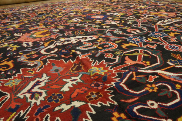 Detailed view of a dark, traditional rug with bright red, blue, and multicolored floral designs.
